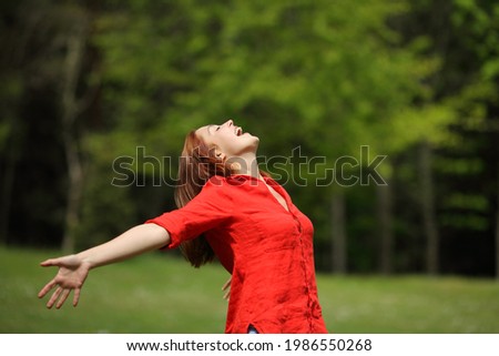 Excited woman in red screaming to the air stretching arms in a forest