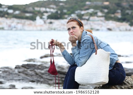Frustrated casual tourist holding bikini complaining on the beach due bad weather