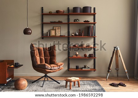 Stylish interior of living room with design brown armchair, wooden bookcase, pendant lamp, carpet decor, picture frames and elegant personal accessories in modern retro home decor. Template.
