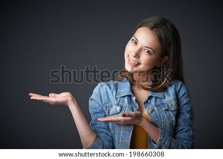 Happy trendy smiling teenager girl showing / holding on the palm blank copy space, over gray background