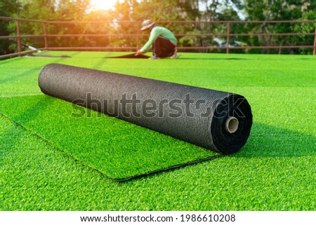Roll of astroturf or field turf matting of artificial grass soccer field,green lawn background with workers pave the counterfeit grass with sunlight background. Royalty-Free Stock Photo #1986610208