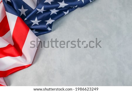 The American flag lies on the left against a cement background with space for text on the right, top view close-up.