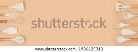 Banner made with cooking utensil set and copy space. Silicone kitchen tools with wooden handle on beige background. Top view Flat lay. Royalty-Free Stock Photo #1986625013