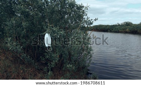 On the bank of the river grows a shrub on which hangs a snush medical mask. Protecting the environment during a pandemic. Soft selective focus.