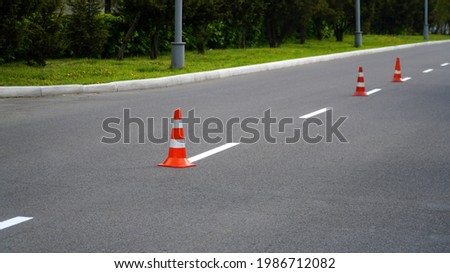 Macro shot of road traffic cones with orange and white stripes standing on street on gray asphalt during road construction works. Just painted white street lines on pedestrian crossing. 