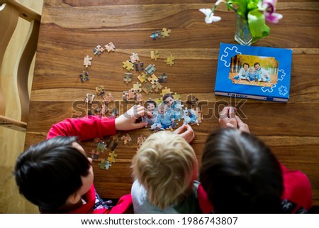 Three children, boys, assembling puzzle with their picture from an autumn forest, playing at home together