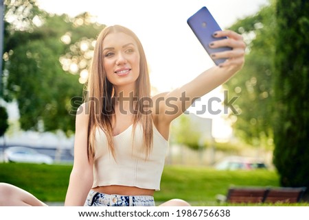Happy smiling blond woman makes selfie by mobile phone,outdoor.Concept of vacation lifestyle. Beautiful girl with smartphone in the park.Sunny day. Happiness concept. High quality photo