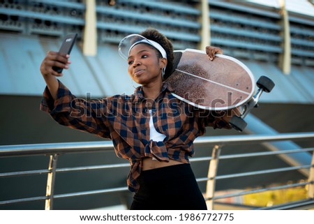 Portrait of happy african-american woman with skateboard. Young stylish woman taking selfie photo