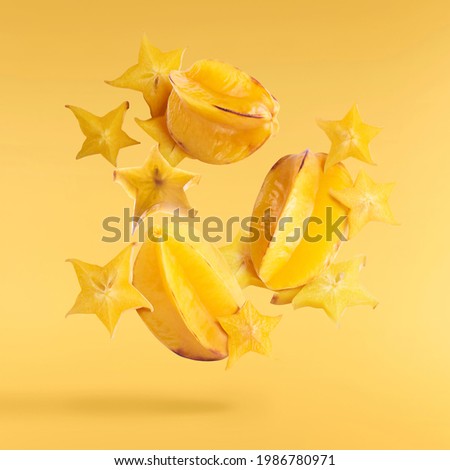 Creative image with fresh ripe yellow carambola or starfruit falling in the air isolated on the yellow illuminating background. Food levitation or zero gravity conception. High resolution image