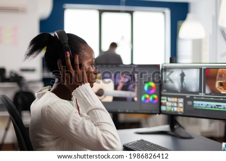 African video editor with headset listening music wihile editing footage and sound sitting in creative agency. Videographer in digital multimedia company processing movie with post production software