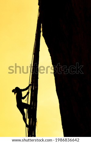 A Bamar bird’s nest collector scaling a cliff by rope and bamboo material at an bird's nest island in Andaman Sea, South Myanmar. Swiftlets nest, Bird's Nest Soup. Silhouette. Focus on a man.