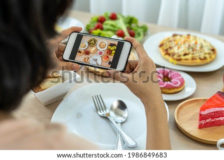 A reviewer's hand using a mobile phone to take pictures of food at a restaurant table.Take photo to write a review of the restaurant to share on the internet.