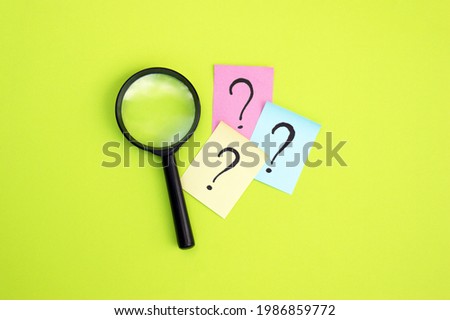 Top view photo of a magnifying glass and sticker with question mark lie on a green background. Search concept.