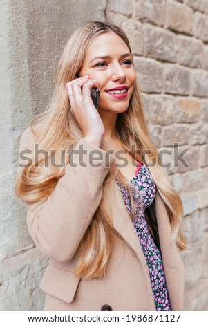 Blond latin woman chatting on mobile phone while leans against the wall in the street