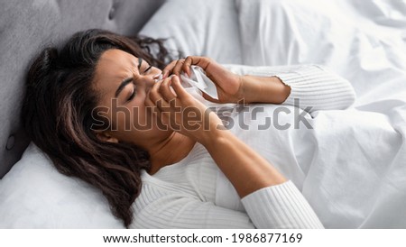 Sick black woman suffering from running stuffy nose and sore throat. Upset ill African American lady lying in bed, blowing her nose using paper napkin tissue, banner. Cold And Flu Concept Royalty-Free Stock Photo #1986877169