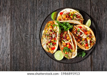 tacos of flour tortilla shells filling with grilled chicken meat, corn, roasted sweet potatoes cubes, red pepper and parsley served on a black plate, flat lay, free space