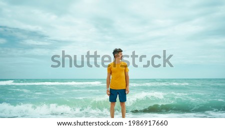 man in yellow shirt standing in sea water with waves, feeling calm and harmony