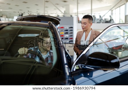 Test drive. Top view of car buyer sitting in auto, choosing new automobile with seller In store. Focus on man.