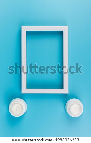 White jar of skin cream and white photo frame on blue background. Place for text. Copy space