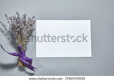 Lavender blossom with white paper sheet mockup on gray background. White paper empty blank, dried flowers on gray table. Invitation card mockup.Flat lay, top view, copy space, mockup
