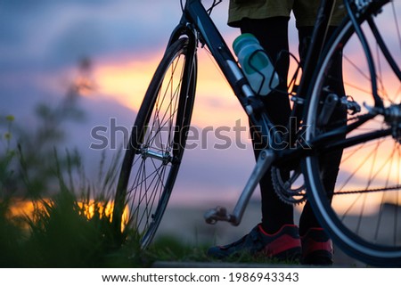 a man stands next to a bicycle on a mountain and looks at the sunset