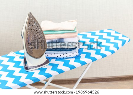 Folded ironed men's shirts lie next to the iron on the ironing board.