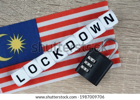 LOCKDOWN wording on a blocks with a black padlocks a over a wooden background an Malaysia flag. Lockdown during pandemic