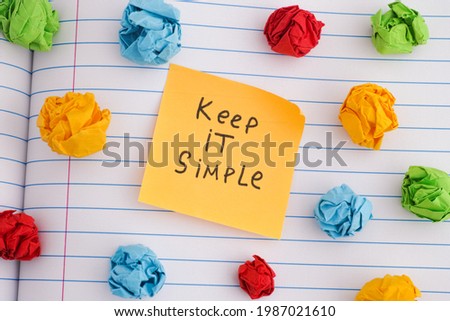 Keep it simple. A yellow paper note with the phrase Keep it simple on it with some colorful crumpled paper balls around it. Close up. Royalty-Free Stock Photo #1987021610