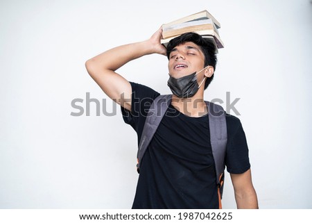 Young Indian boy holding books on his head, wearing mask, and getting ready for college after the corona virus lockdown is over.