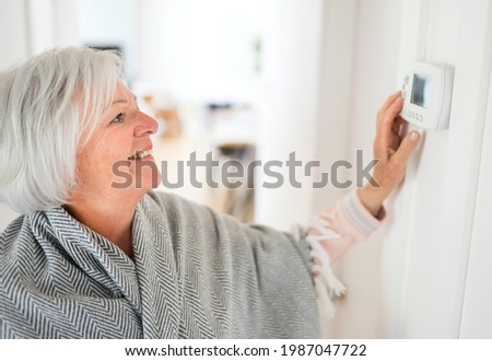 A Senior woman adjusting her thermostat at home Royalty-Free Stock Photo #1987047722