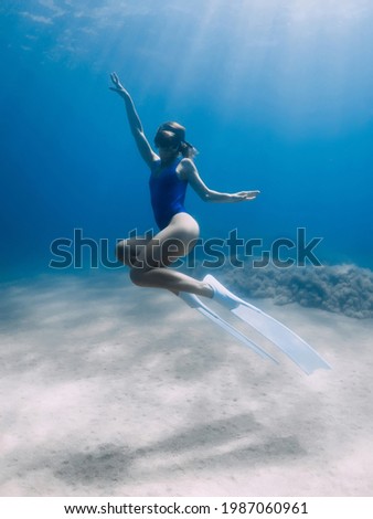 Lady freediver with fins posing and glides underwater in ocean with sunlight. Freediving in warm water