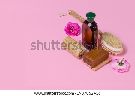 Natural soap, loofah, massage brush and bottle of cosmetic product on a pink background with roses with copy space. Natural organic cosmetics for face and body. Skin care concept.