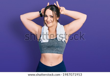Young hispanic girl wearing sportswear and towel posing funny and crazy with fingers on head as bunny ears, smiling cheerful 