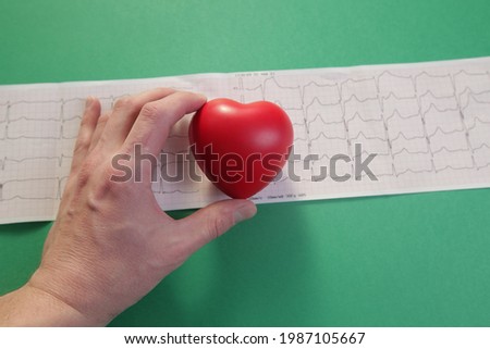 Doctor's hand with red heart and cardiogram on green background