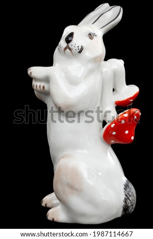 Porcelain figurine of a hare carrying amanita mushrooms, isolated on black background