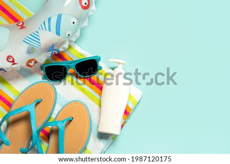 Summer holiday concept.Top view of blue flip flops,beach towel, blue sunglasses,bottle of sunscreen and float with copy space on a blue background