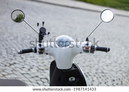 The steering wheel of a moped on the background of a cobbled road. Motor scooter steering wheel and background with space for text Royalty-Free Stock Photo #1987141433