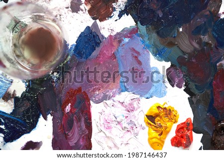 A palette with multi-colored paint and a glass with oil. High quality photo