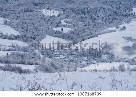 Snow-covered village in the mountains in the early morning with creeping smoke from the chimney