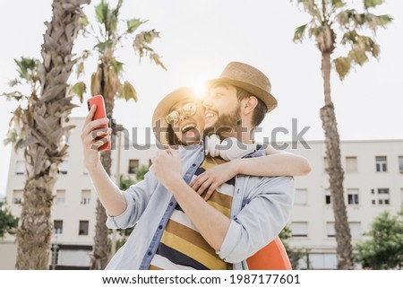 Happy couple having fun doing selfie during summer vacation with palm trees in background - Lovers lifestyle, travel concept - Soft focus on woman face