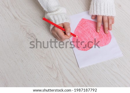 Child's hands close up drawing a red heart on a light background. Copy space for text