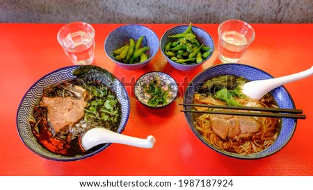 Picture of two bowls of ramen (japanese hot soup) served in nice blue painted bowls on a bright red table.