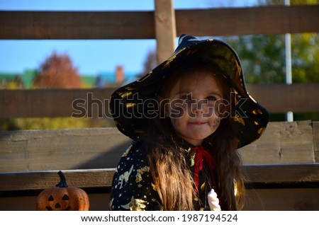 a girl in a witch suit and a black hat on the head with black Halloween make-up, zombie eating sweets jelly worms at a celebration of Halloween