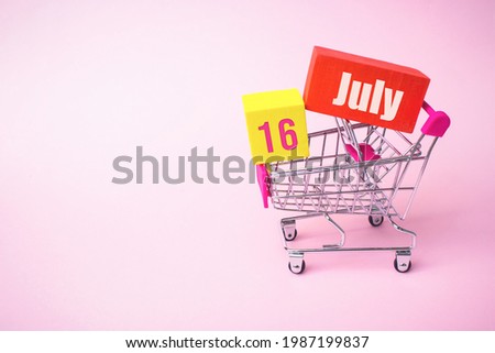 July 16th. Day 16 of month, Calendar date. Close up toy metal shopping cart with red and yellow box inside with Calendar date on pink background. Summer month, day of the year concept