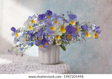 A bouquet of pansies and forget-me-not flowers in a vase on the table. Blur, selective focus.