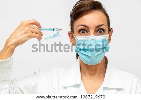doctor with wide eyes and scared face, holding a syringe with a needle and pointed at her head