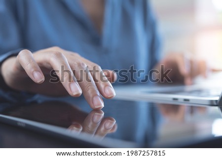 Close up of woman hand using digital tablet, finger touching on screen and working on laptop computer on table at home office, modern technology, online working, telecommuting concept