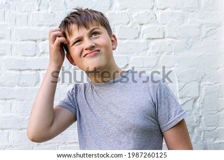 Pensive smiling boy is wistfully scratching his head. schoolboy remember something, having thoughts. Thinking concept Royalty-Free Stock Photo #1987260125