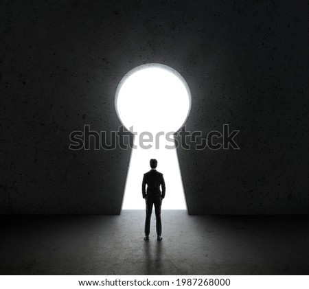 Businessman standing in front of bright big keyhole door Royalty-Free Stock Photo #1987268000