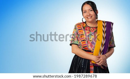 Smiling indigenous woman looking at the camera, wearing a colourful dress on a blue background.